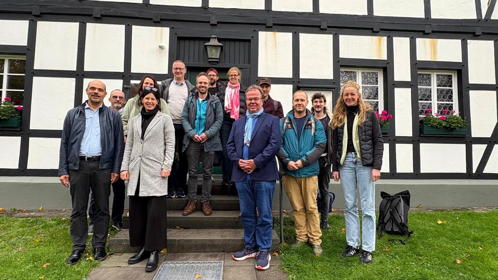 Das Bild zeigt eine Gruppe von Personen, die sich vor einem Fachwerkhaus versammelt haben. 